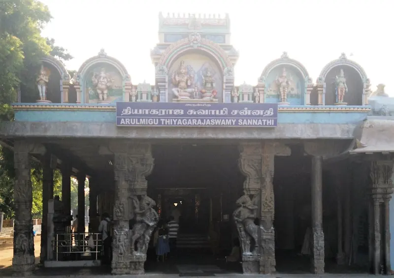 A pillared porch with a name board in Tamil and English, painted figures above and two carved guardians