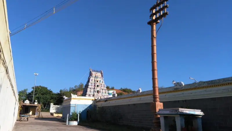 A tall copper-coloured flagstaff beside a long wall with bull figures on top, and a tower far behind