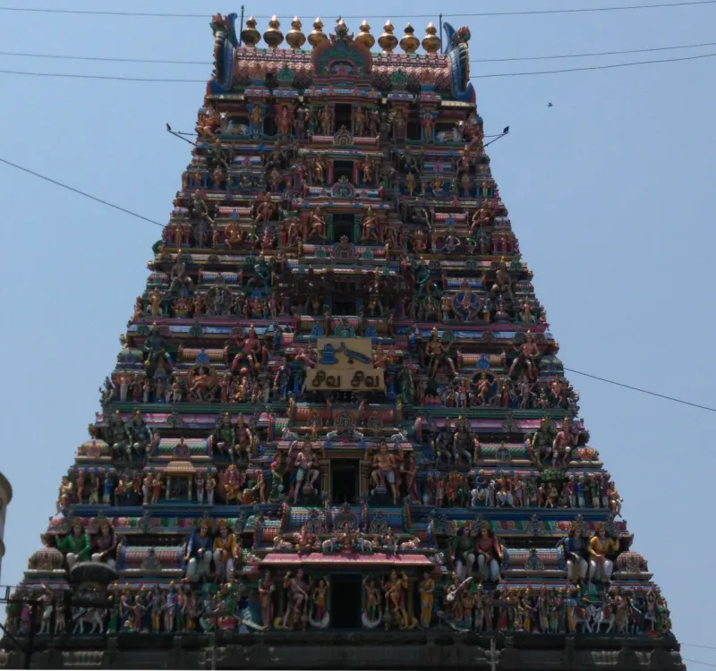 A tall tiered tower seen from below, crowded with painted figures on every level, against a blue sky.