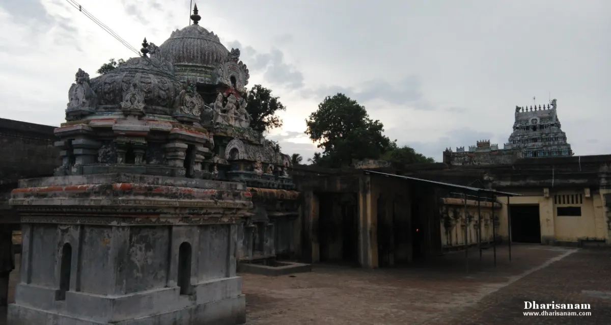 A weathered stone shrine tower with carved figures in a courtyard, and a tall painted tower in the distance.