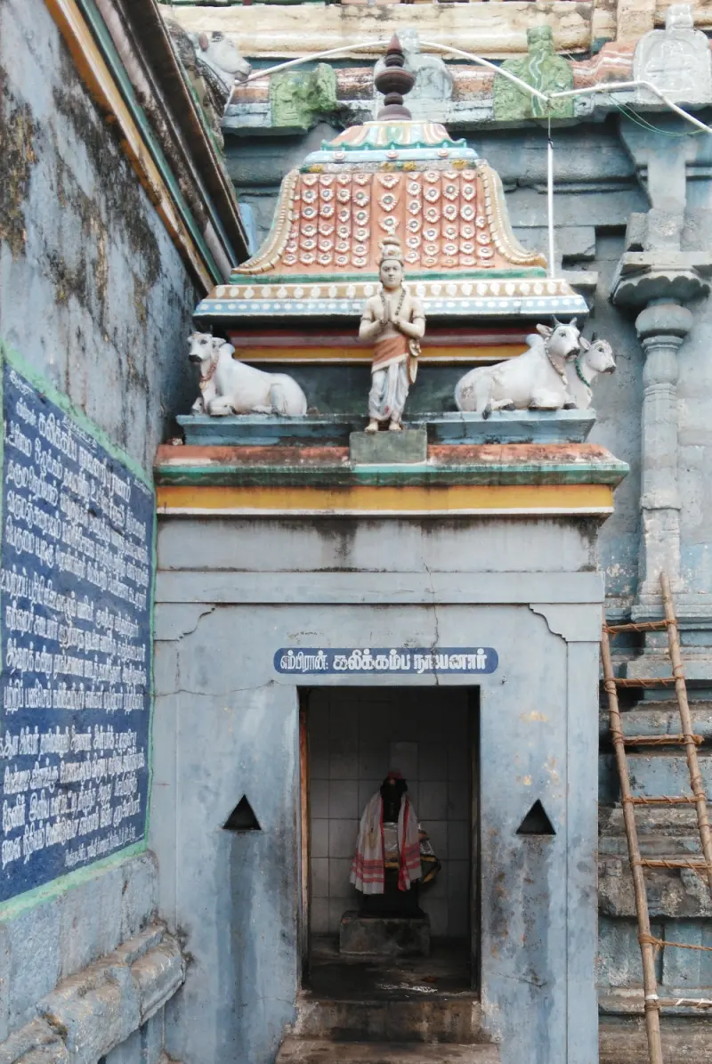 Small shrine with painted bulls and a standing figure above, and a Tamil inscription board beside it