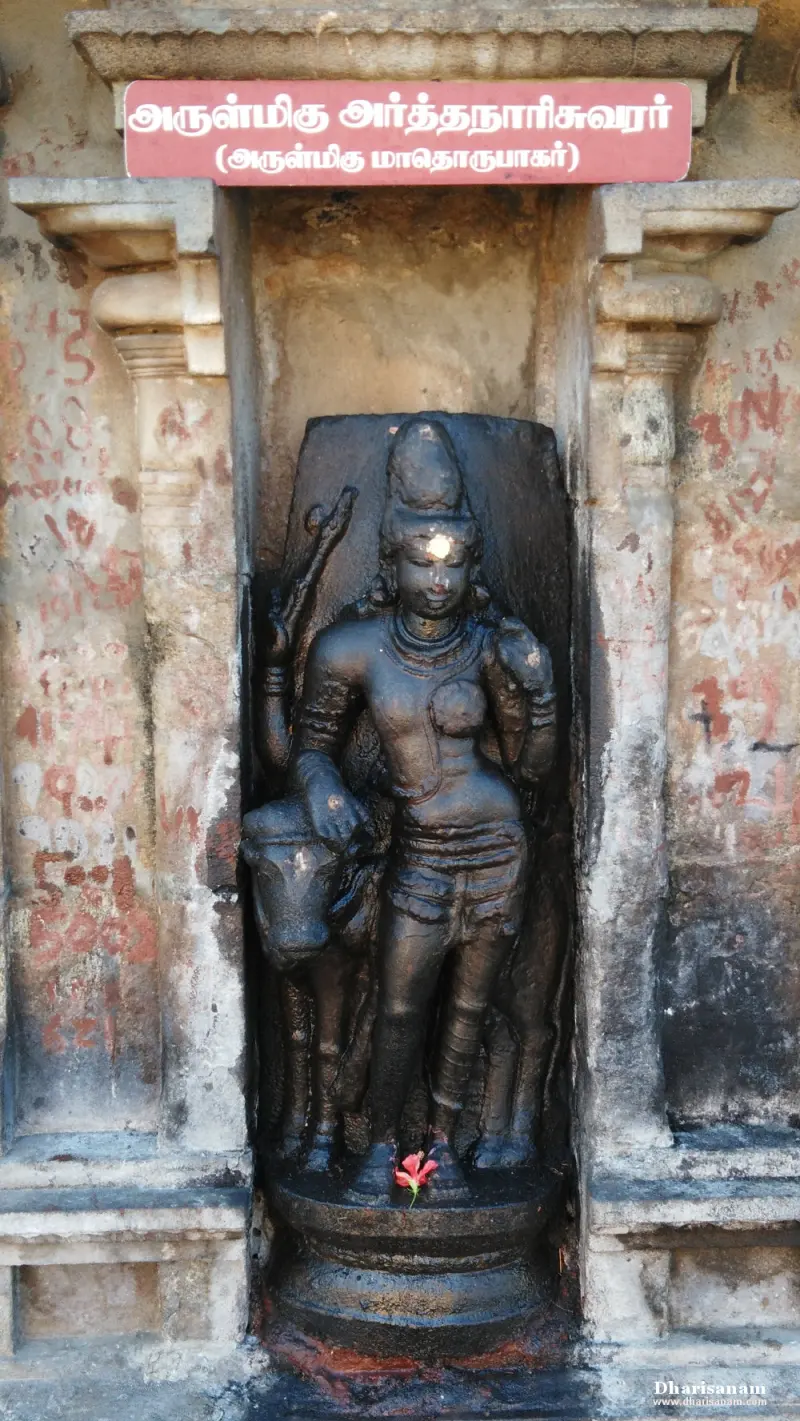 A black stone Arthanareeswarar standing beside a bull, under a Tamil name board
