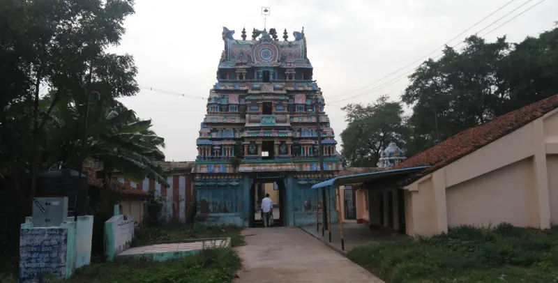 A painted gopuram over the entrance, seen along a paved path with trees on both sides.