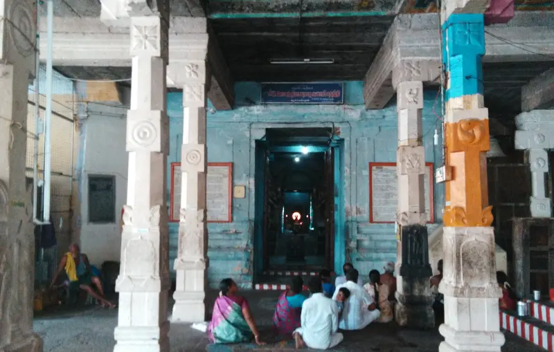 Devotees seated in a pillared hall facing a lit doorway at the far end