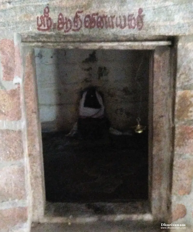 A small stone shrine with a dim idol in a white cloth inside, with its Tamil name painted above the door
