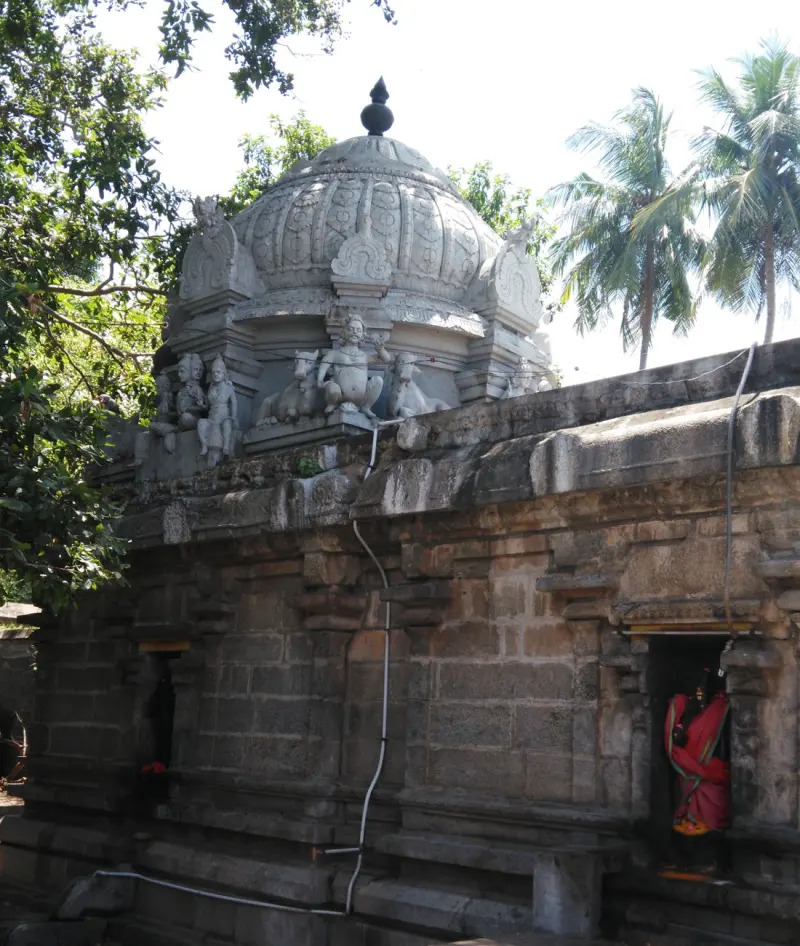 A stone shrine with a domed tower, carved figures and bulls, and a deity in red cloth in a doorway at right.