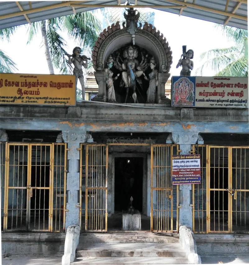 A small shrine behind yellow metal gates, with a figure and two attendants in a niche above the doorway