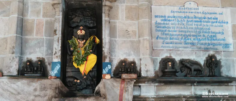 Garlanded black stone idol in a niche, with small idols and a Tamil plaque beside it