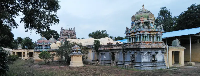 A wide view of a grassy courtyard with a domed sanctum tower, small shrines and the gopuram in the distance.
