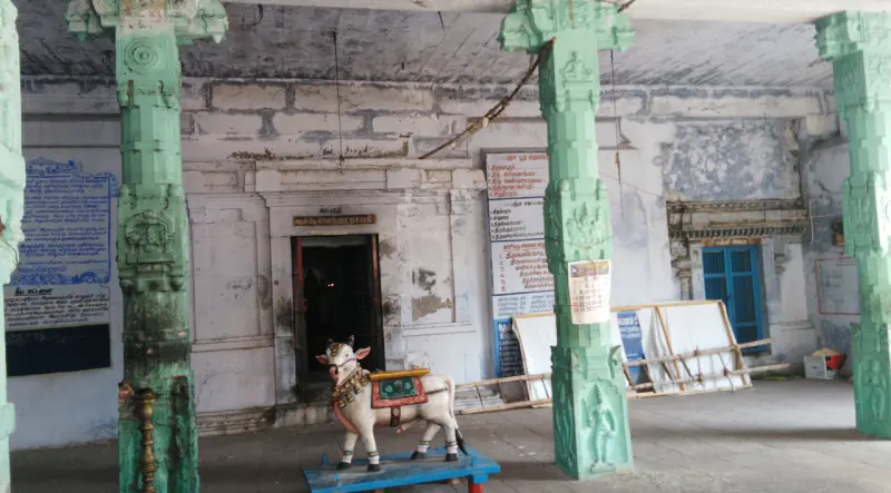 A pillared hall with notice boards on the wall and a white Nandi figure on a blue stand