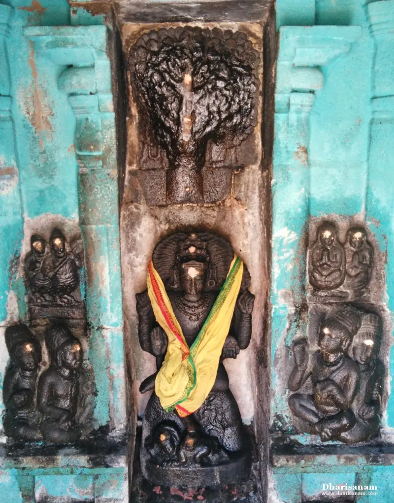 A seated stone Dakshinamurthy in a niche with a yellow cloth, a tree carved above and disciples on either side