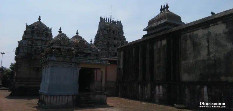 Carved shrine roofs in front of a darker stone tower, beside a long temple wall