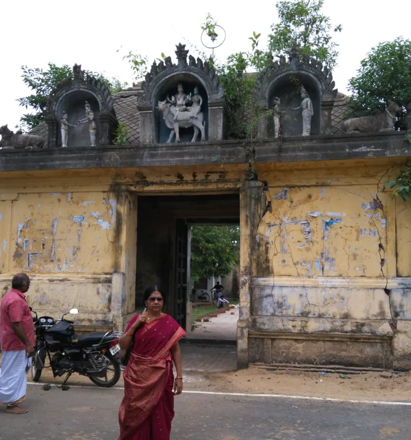 A yellow gateway with three stucco niches above it, seen from the road, with a motorcycle parked beside
