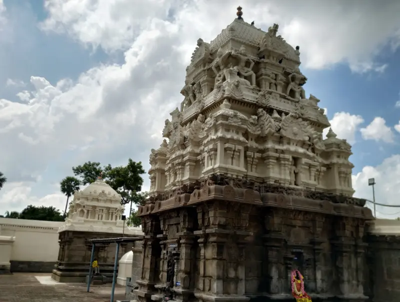 A tiered stone tower with many carved figures rising above a stone base, with another small tower at the left.