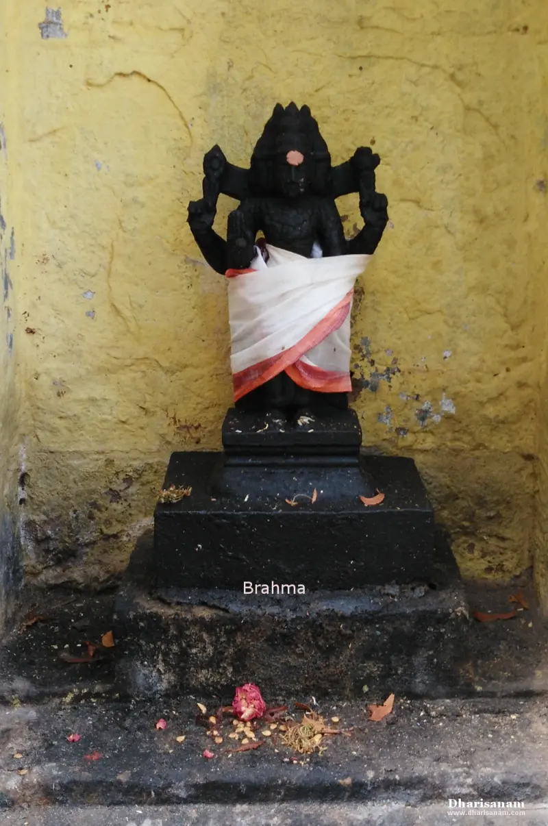 A dark Brahma idol draped in white cloth against a yellow wall