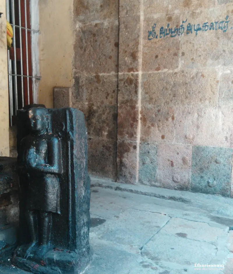 A dark stone figure carved on a pillar beside the corridor wall, with Sri Apputhi Adigalar written above it