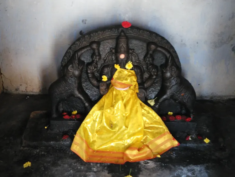 Dark stone idol dressed in yellow cloth and flowers, with an elephant on each side
