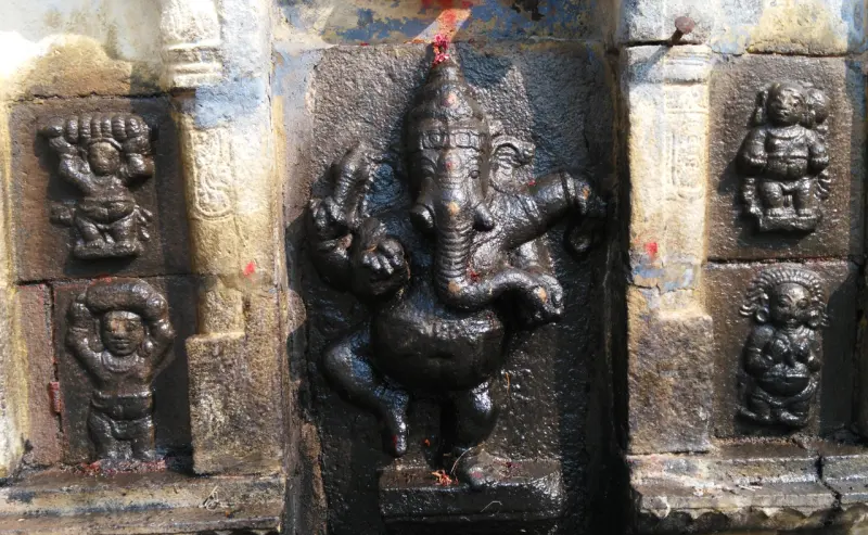 A dark stone relief of a dancing, elephant-headed figure with a small figure on each side.