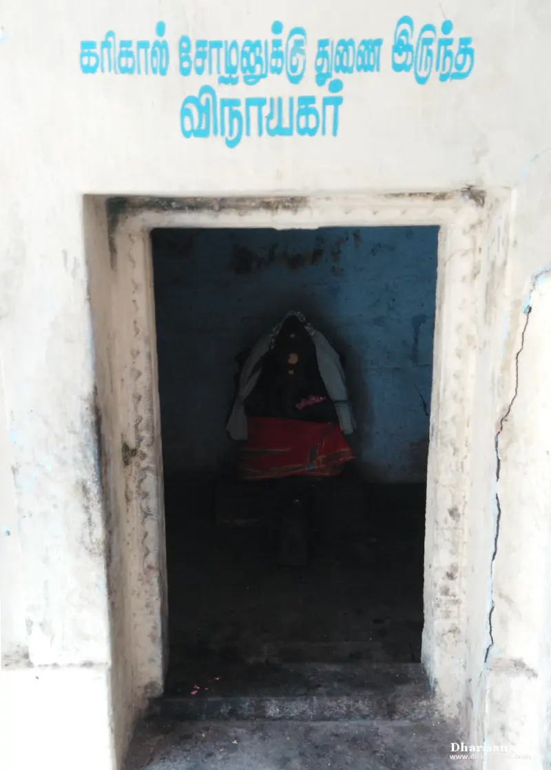 Small dark doorway under a blue Tamil name, with an idol in red cloth seated inside