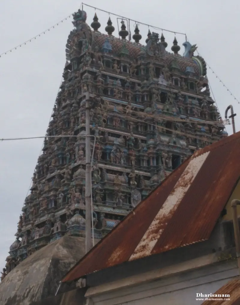 A multi-tiered tower covered in painted figures, with a rusted tin roof in the foreground and strings of lights