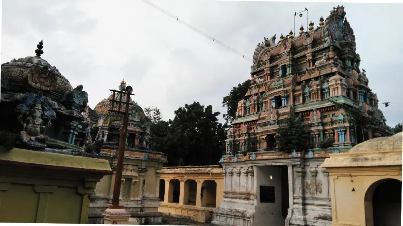 A tall coloured gopuram rises behind pillared halls and a domed tower; a flagstaff stands in front.