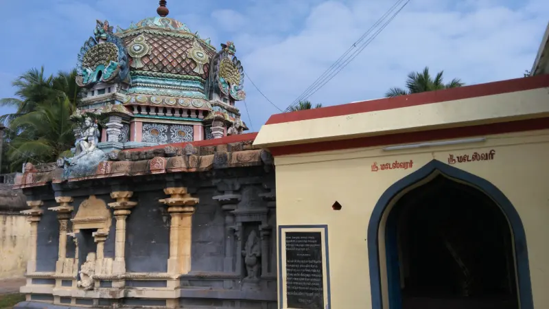 A yellow building with a pointed arched door and two Tamil name boards, beside a stone shrine with a painted dome.