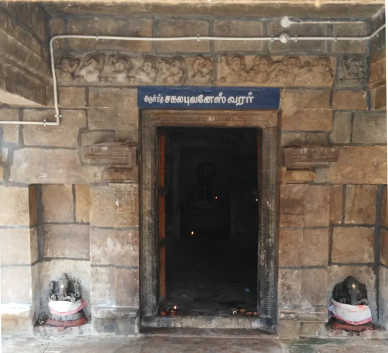 Stone doorway with a blue Tamil name board, lit lamps inside, and a small Vinayakar idol on each side