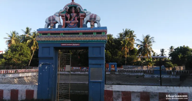 A blue arched gateway topped with a goddess figure and two elephants, beside a tank with red and white steps.
