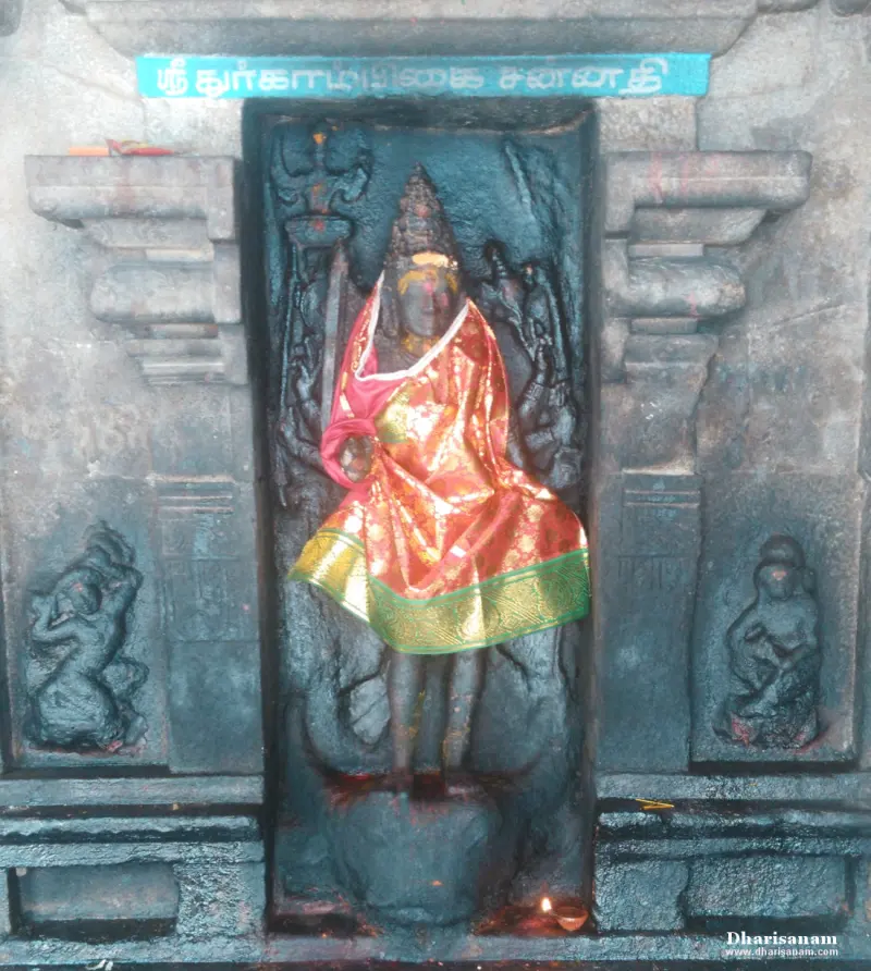 Black stone Durgai idol draped in an orange silk cloth, in a niche with a lit lamp