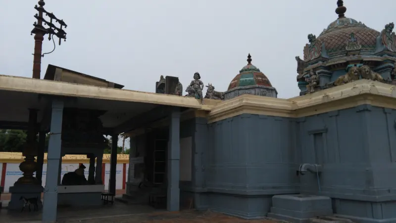 A grey sanctum wall with domed roof at right and the open mandapam with flagstaff and Nandi at left.