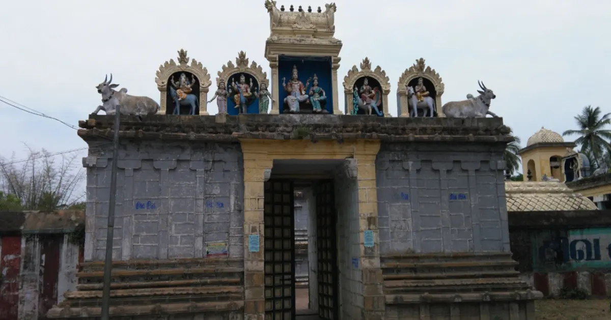 A grey stone gateway with a dark doorway, painted figures in arched niches and two bull statues on its roof.