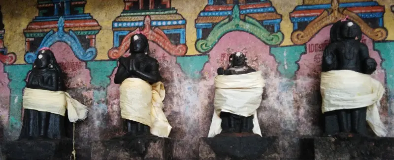 Four dark stone idols draped in cloth against a painted wall
