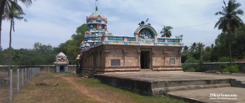 Stone shrine on a raised base with a painted roof, with a small shrine to its left and palm trees behind