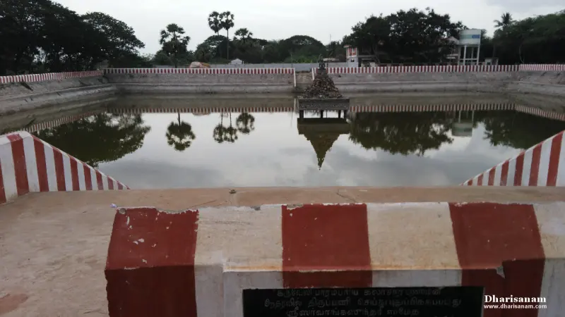 A temple tank with red-and-white striped steps and a small structure at the centre of the far side