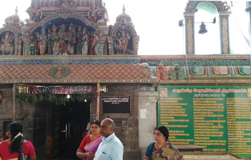 A shrine doorway under a painted tower, with a green Tamil information board at right.