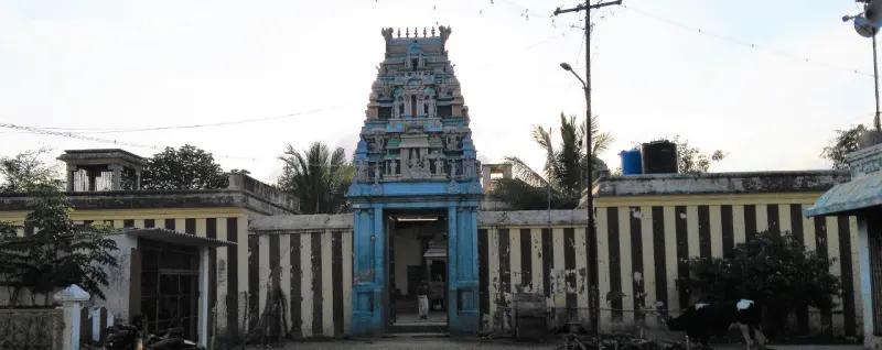 A blue entrance tower with a painted top, set in striped compound walls; a cow stands in front.
