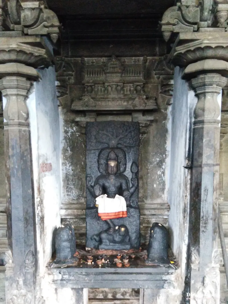 Seated stone idol in a pillared niche with a lingam on each side and small lamps lit