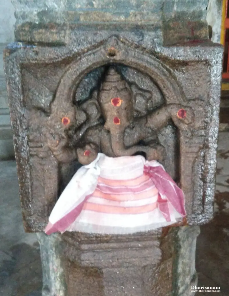A Vinayakar figure carved in an arched niche on a pillar, with red marks and a striped cloth across the lower part