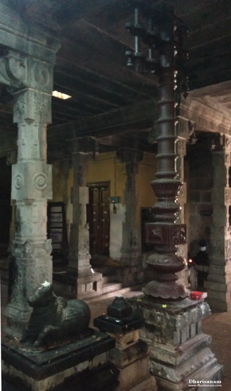 Stone Nandi and tall flagstaff among carved pillars in a dim hall