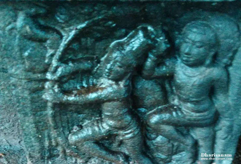 Dark carved relief of figures, one drawing a bow, beside another seated figure