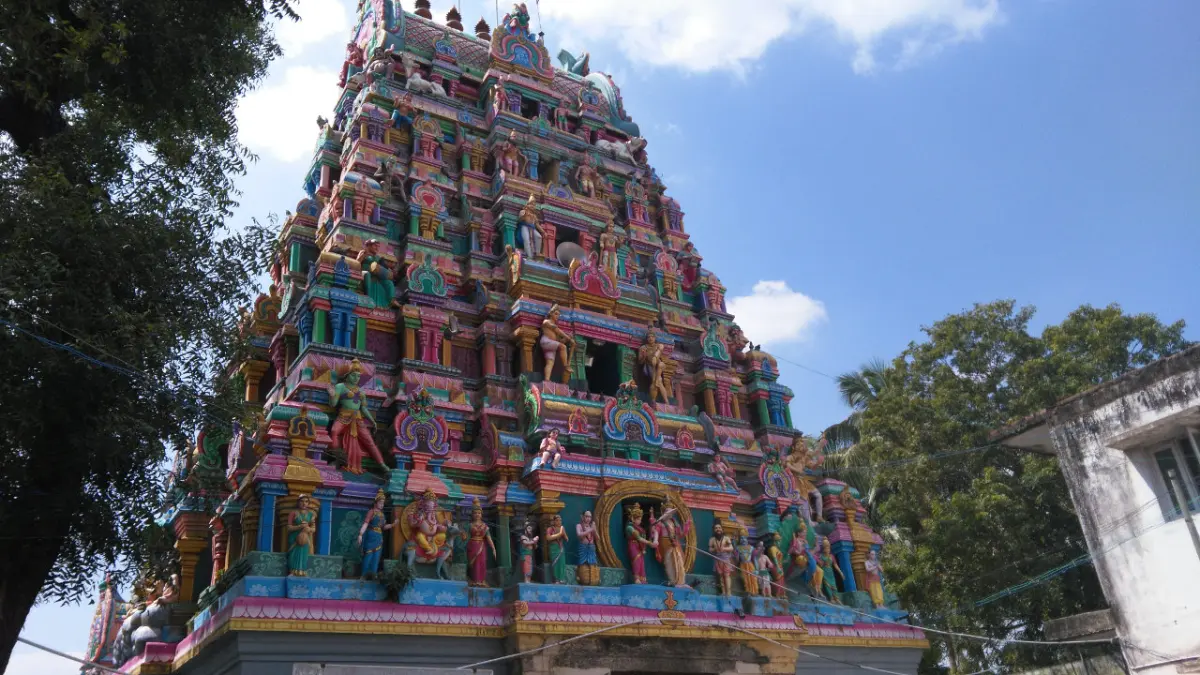 The painted tower rises in tiers of coloured figures against a blue sky, with trees at left and a building at right.
