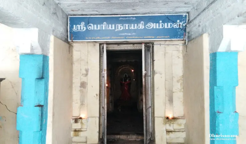 Doorway under a blue Tamil name board with lit lamps at its sides and an idol in red visible inside