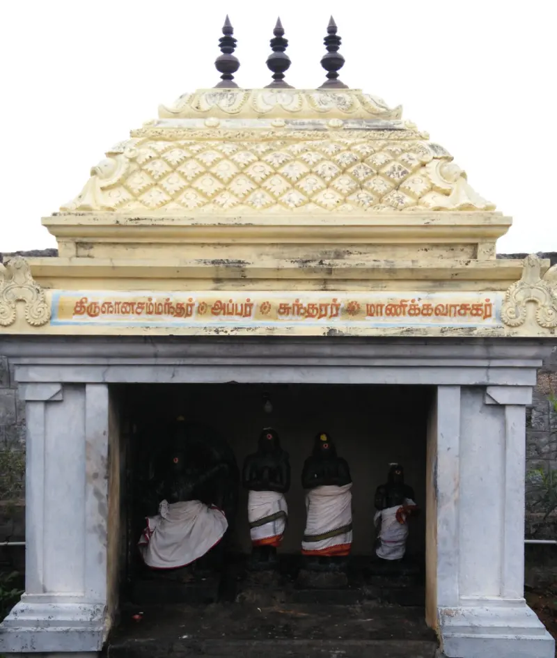 A small shrine with a patterned roof and a name board naming four saints, with four dark figures in white cloth inside.