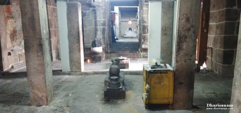 Stone pillars in a dim hall with a small lingam and a yellow box in front and a lit lamp far ahead