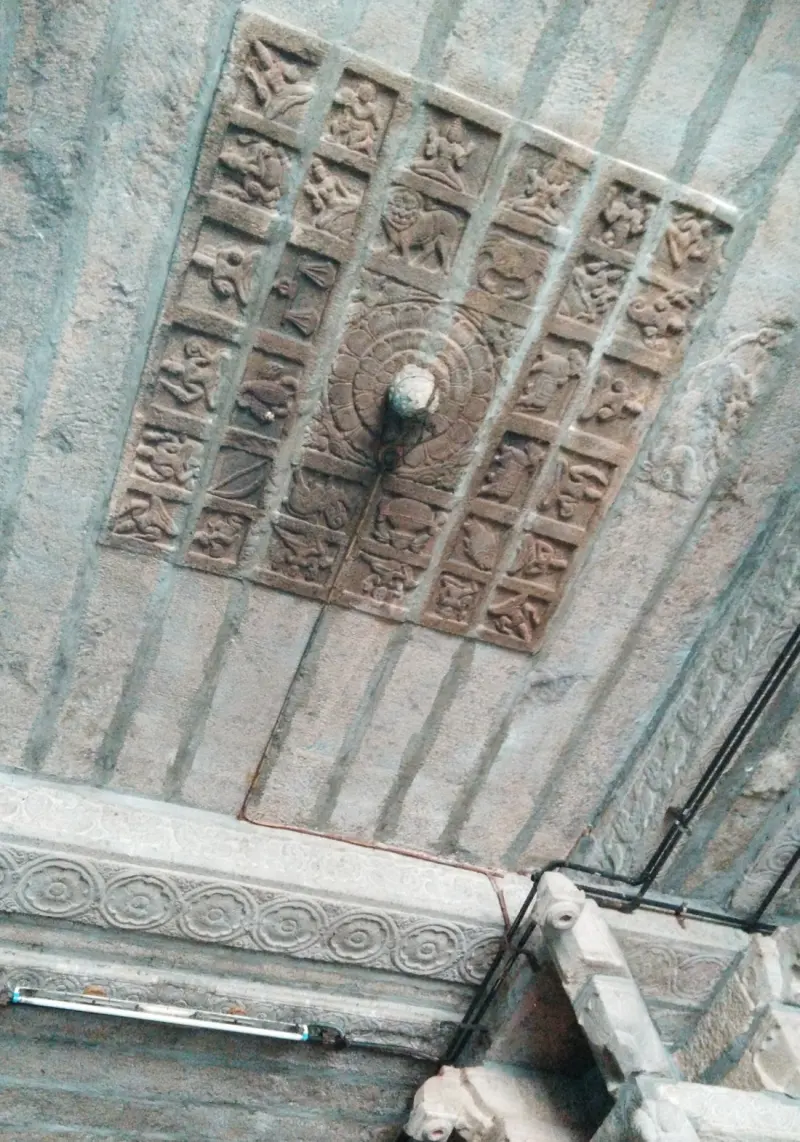 A square panel of carved patterns set in the stone ceiling of a corridor, with a hook at its centre