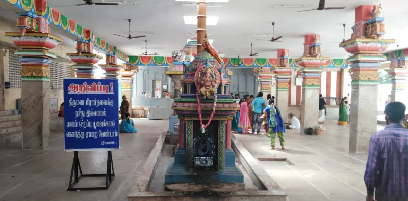 A small shrine with a garlanded Ganapathy idol in the hall; a blue Tamil notice board stands at left.