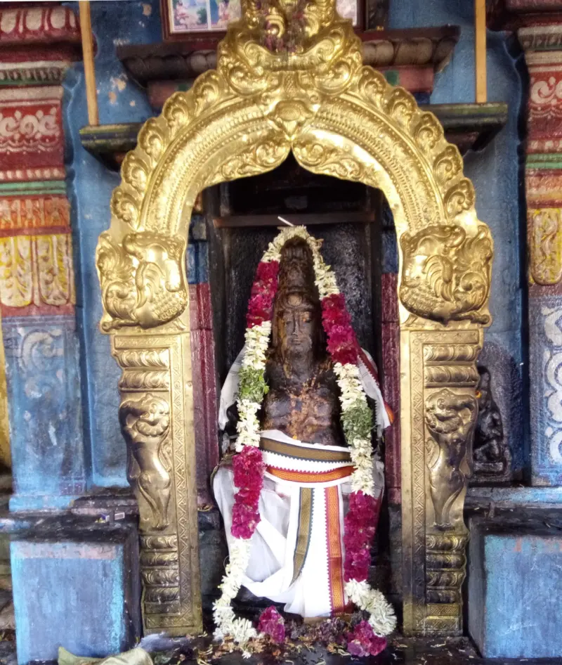 Stone image in a white dhoti and flower garlands, framed by a gilded arch