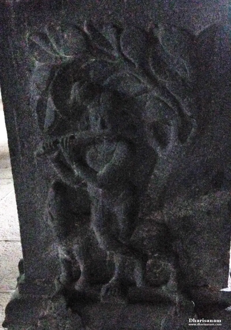 A dimly lit stone relief of a standing figure holding a flute, with leaves above