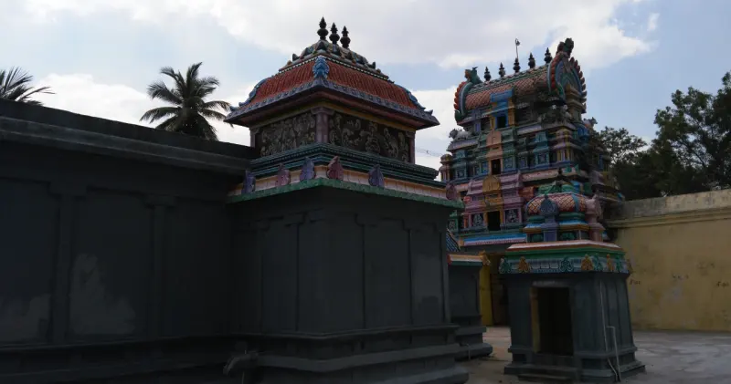 A dark stone shrine wall with a small painted tower, and a larger tiered tower behind it on the right