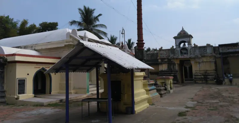 A paved courtyard with a roofed shelter and a yellow shrine; the red flagstaff and a long stone wall stand behind.